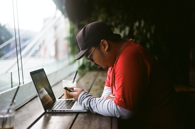 man looking at his phone next to the laptop